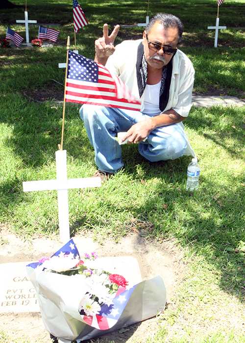 After the Memorial Day tribute concluded at the Downey Cemetery on May 27, Anthony Munoz puts up a peace sign as he kneels by the grave of his uncle, Gabino Munoz, to remember and acknowledge his legacy. Gabino Munoz was wounded in action in Germany during WWII, and received a Purple Heart.